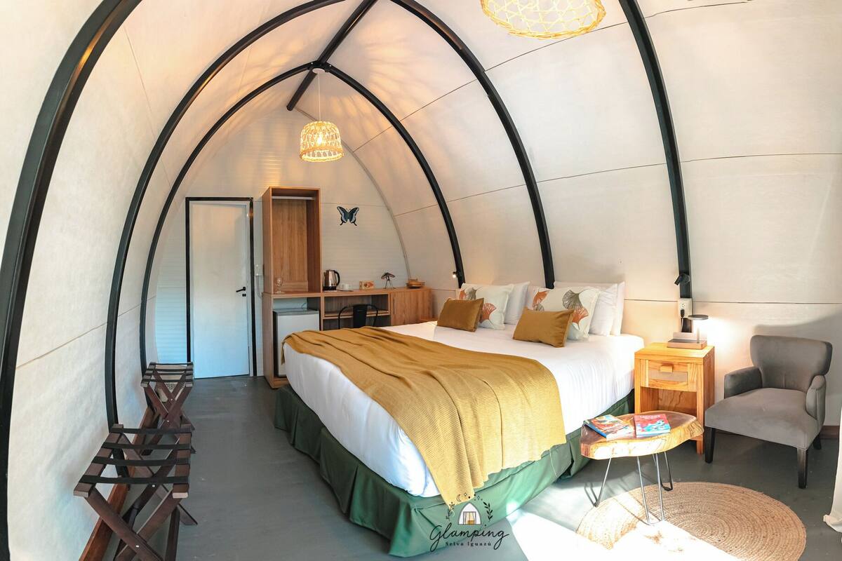 A cozy, arched room with a bed, a desk, a chair, and a small table with books.