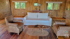 Una habitación acogedora con un sofá blanco, dos sillones marrones, una mesa de centro de madera y un televisor pequeño sobre un mueble de madera.