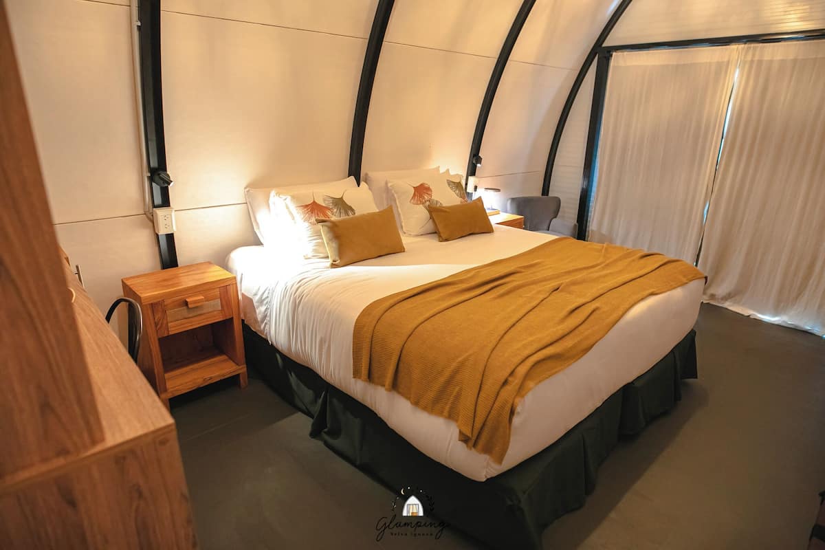A cozy bedroom with a large bed, a wooden nightstand, and a curved ceiling.