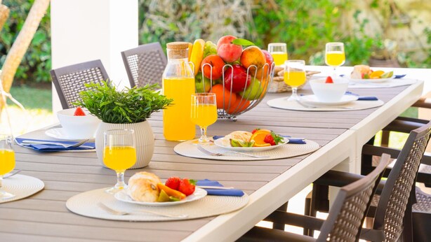 A long dining table set with plates, glasses, and a fruit bowl.