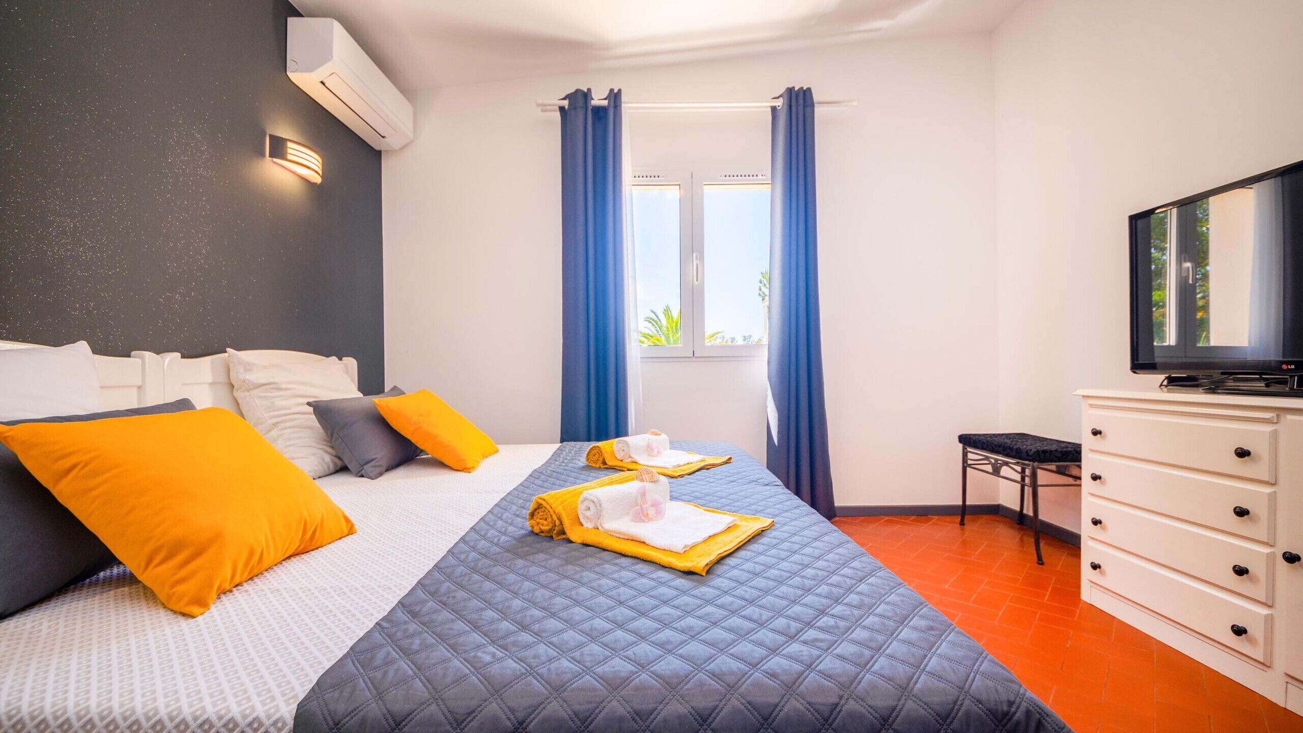 Una habitación de hotel con cama, televisión, cómoda y ventana con cortinas.