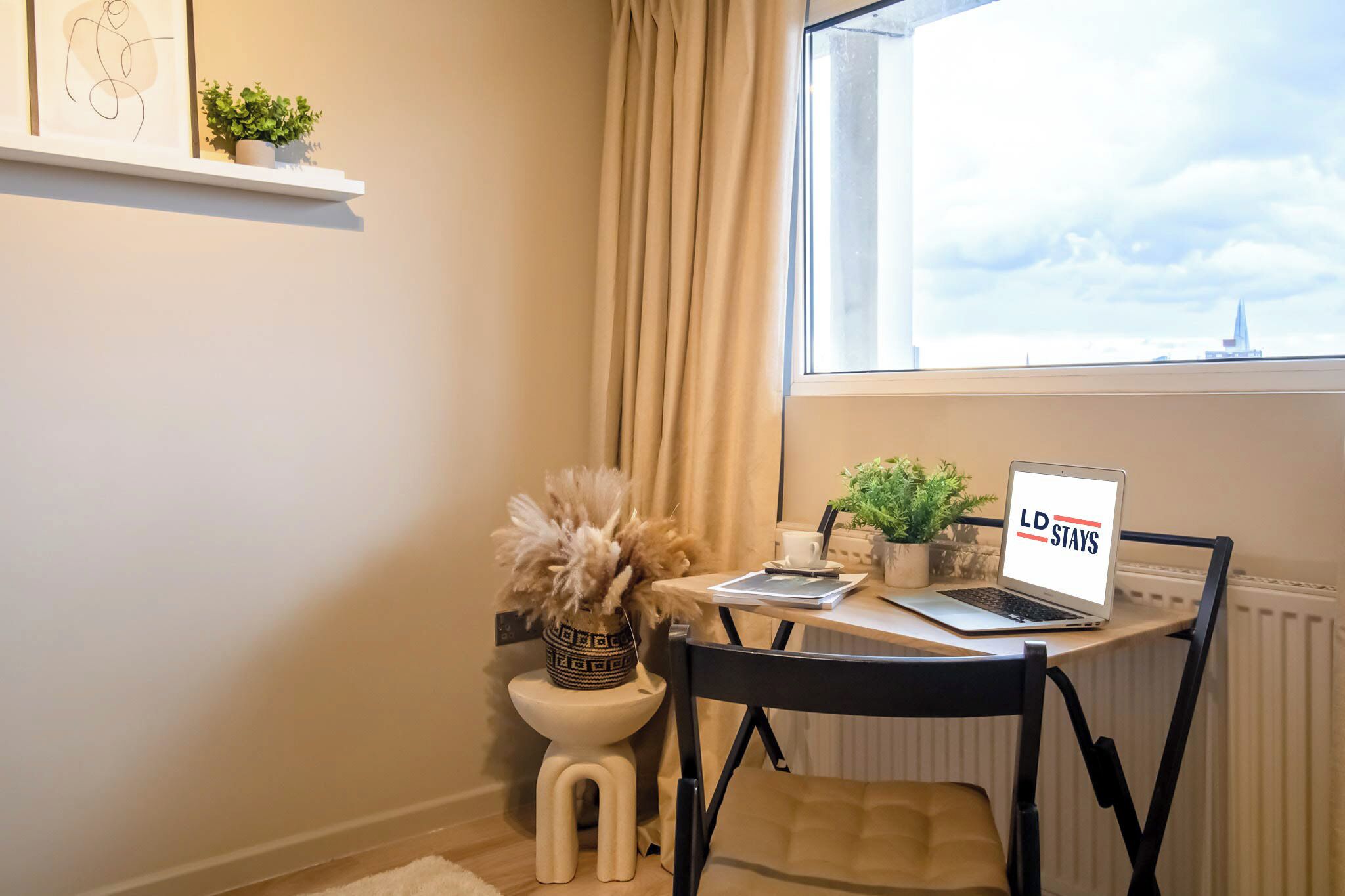 Un espacio de trabajo pequeño con una computadora portátil, una planta en maceta y un jarrón decorativo.