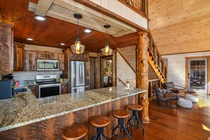 A spacious kitchen with granite countertops, stainless steel appliances, and wooden bar stools. - Sweeping Mountain Views! Secluded, Fire pit, Hot tub, Gas Fireplaces, Game Room! (Mineral Bluff)
