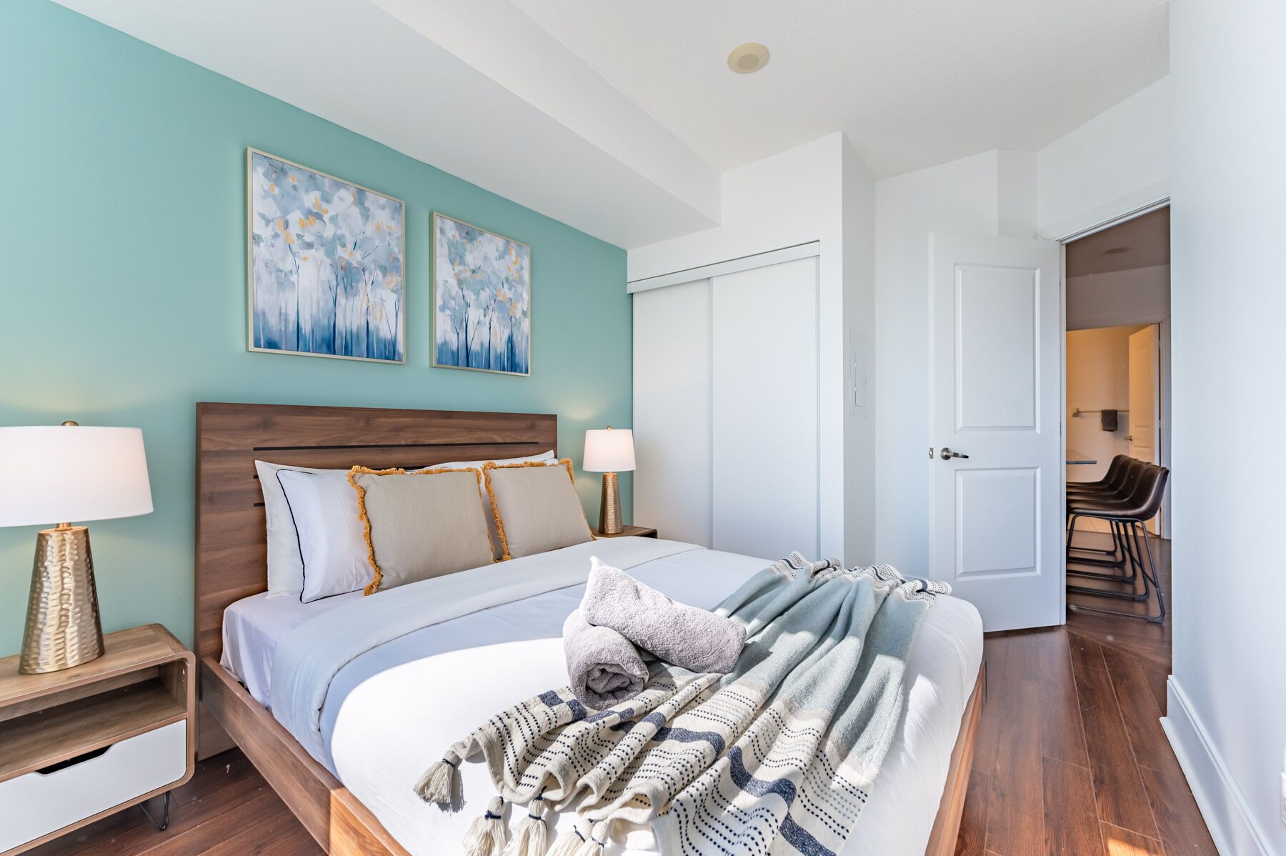 Une chambre moderne avec une tête de lit en bois, deux lampes de chevet, un lit avec de nombreux oreillers et deux tableaux abstraits accrochés au mur.