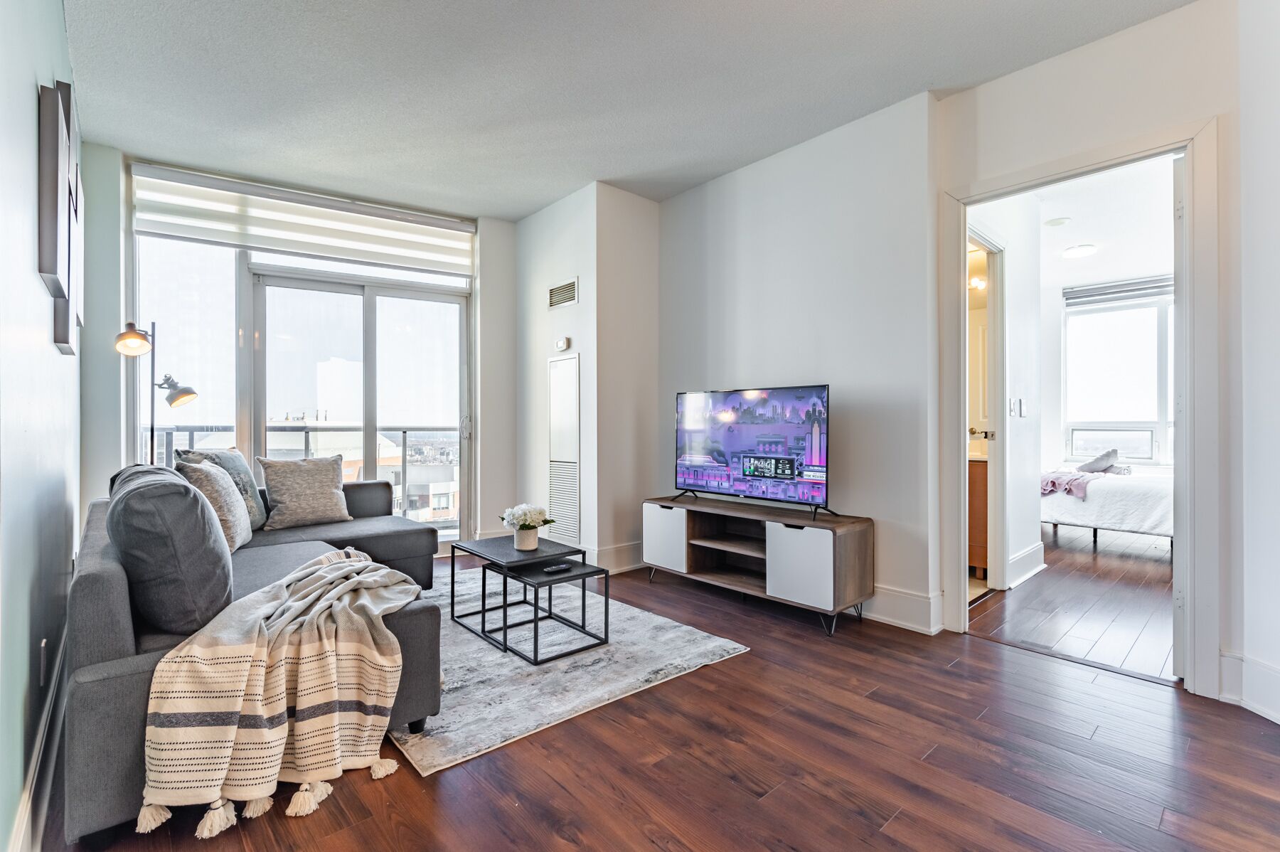 A modern living room with a grey sofa, a coffee table, a TV, and a large window.