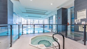 A modern indoor swimming pool with a glass barrier, a hot tub, and clear signage for safety and amenities.