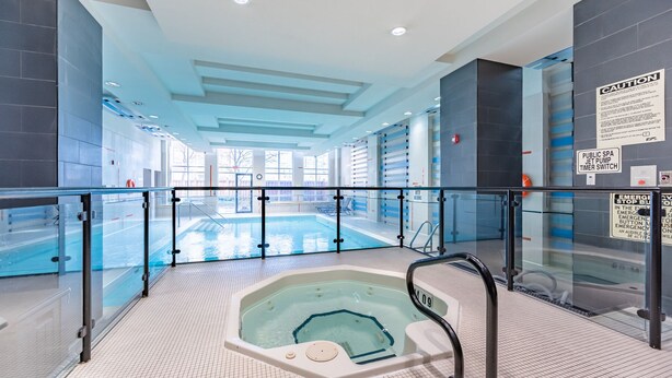 Une piscine intérieure moderne, dotée d’une paroi en verre, d’un jacuzzi et d’une signalisation claire indiquant les consignes de sécurité et les équipements disponibles.