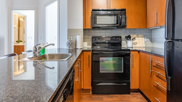 A modern kitchen with wooden cabinets, a stainless steel sink, a black refrigerator, a microwave, and a stove.