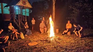 A group of people gathered around a campfire in an outdoor setting with a building in the background. - Amazon Nativo Lodge (Indiana)