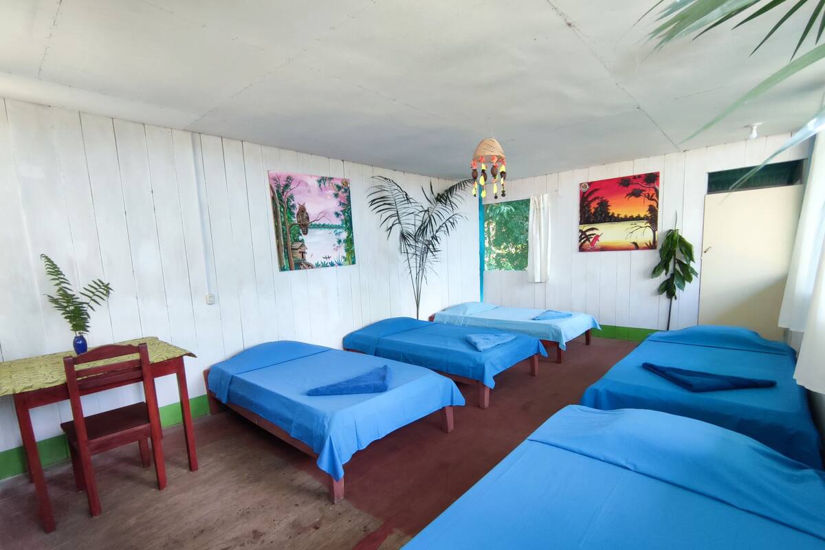 Una habitación con cuatro camas, una mesa de madera y una silla.