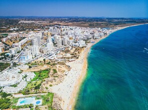 An aerial view of a coastal city with dense high-rise buildings, a sandy beach, and a clear blue sea. - ARMAÇÃO DE PÊRA OCEAN TERRACE by HOMING (Armação de Pêra)