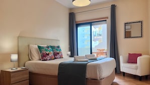 Et hotelværelse med seng, sengeborde, en stol, en balkon og udsigt.
