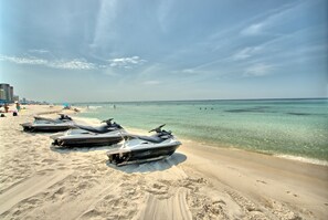 Une plage de sable où sont alignés des jet-skis, offrant une vue dégagée sur l’océan.