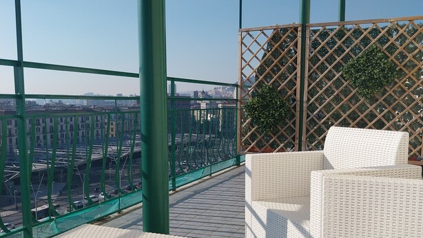 A rooftop terrace with wicker furniture, a view of the cityscape, and a green metal railing. - Attico Central Station Napoli (Naples)