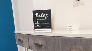A modern room with a grey upholstered bench, a white counter with a 'Relax and enjoy the WiFi' sign, and a marble-patterned floor. - Attico Central Station Napoli (Naples)