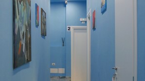 A hallway with blue walls, a marble floor, and artwork. There is a door with a number '2' sign above it. - Attico Central Station Napoli (Naples)