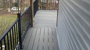 A wooden deck with a black railing, leading to a covered porch area.