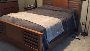 A bedroom with a wooden bed, a nightstand, a lamp, and a dresser.