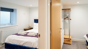 A bedroom with a bed, a bedside table, a window, a radiator, a wooden wardrobe, and a hanging wardrobe.