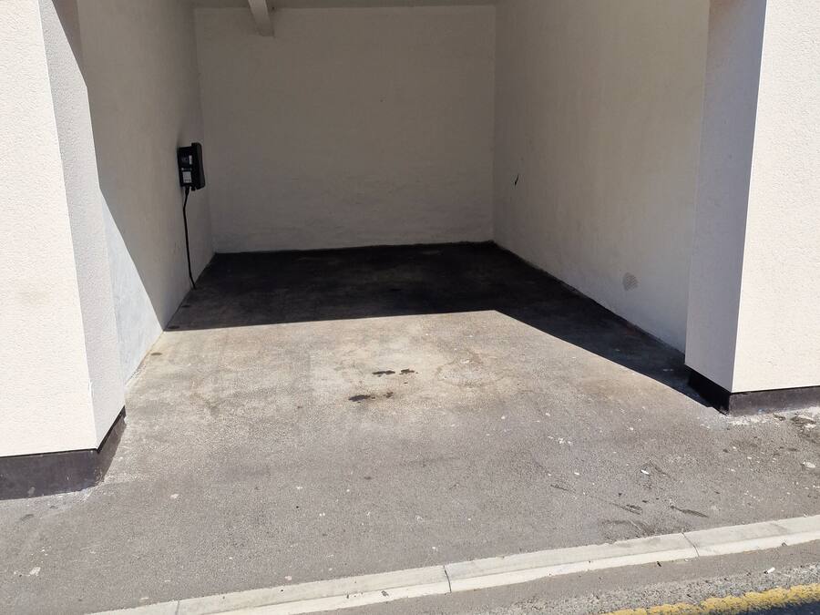 A parking area with a concrete floor and a white wall.