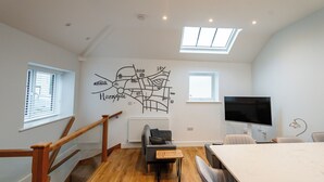 A modern living room with a wooden floor, a sofa, a coffee table, a TV, and a map mural on the wall.