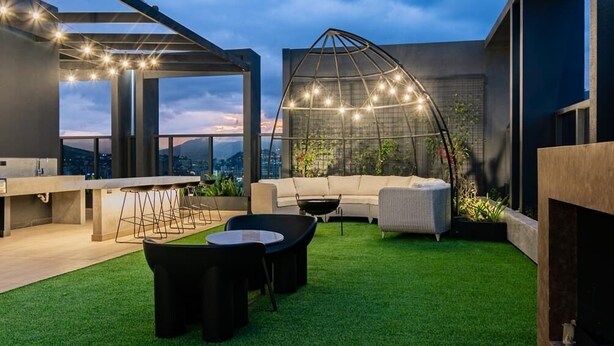 An outdoor rooftop terrace with a seating area, a greenhouse structure, and a city view.