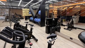 A modern gym with multiple exercise machines, including stationary bikes and treadmills, and a mirrored wall reflecting the equipment.