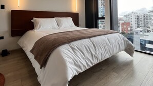 A modern hotel room with a large bed, a view of the city, and a wooden headboard.