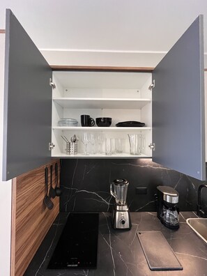 Eine kompakte Küche mit integriertem Mixer, einer Kaffeemaschine und einer schwarzen Arbeitsplatte.