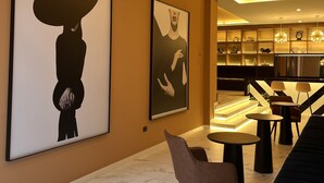 A modern lobby with marble flooring, contemporary artwork, and a seating area with tables and chairs.