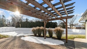 A covered patio area with a brick floor and wooden pergola structure. - Fireplace|Garage|Pets|King Bed! (Green Bay)