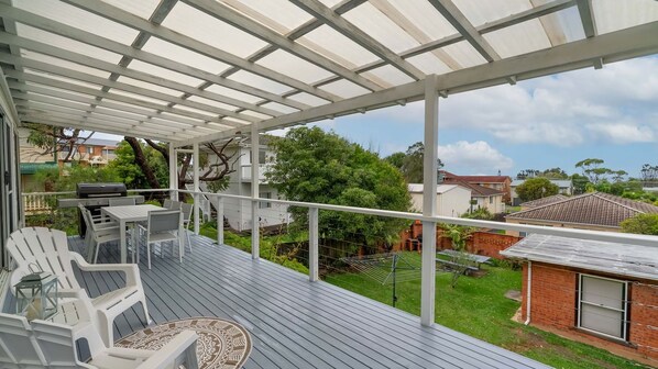 Une terrasse extérieure couverte, dotée d’une table et de chaises, qui offre une vue sur un quartier résidentiel.