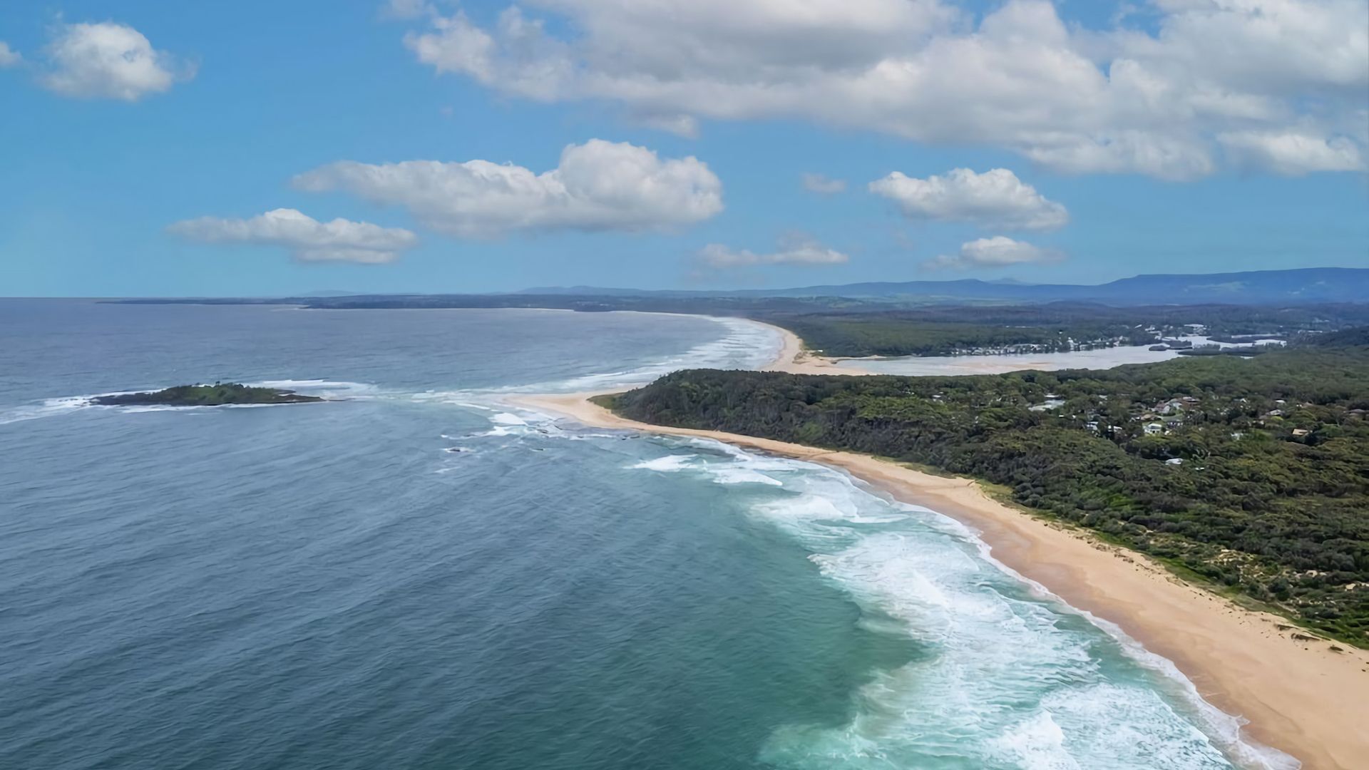 A coastal landscape with a beach, forested area, and a clear sky.