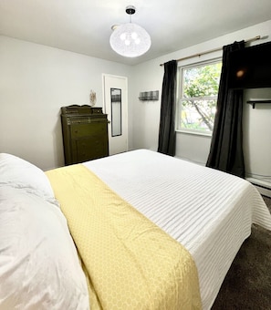 A bedroom with a bed, a dresser, a mirror, and a window with curtains.