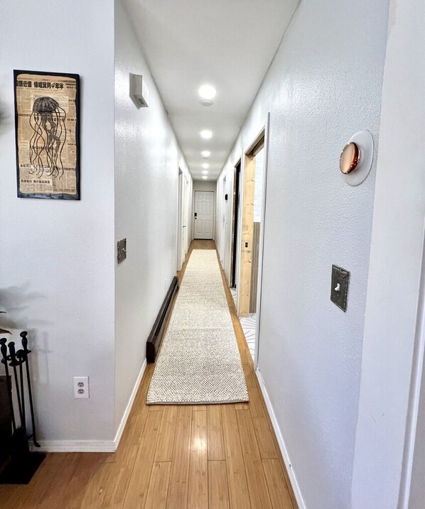 A hallway with a wooden floor, a white carpet, and a wall-mounted light fixture.