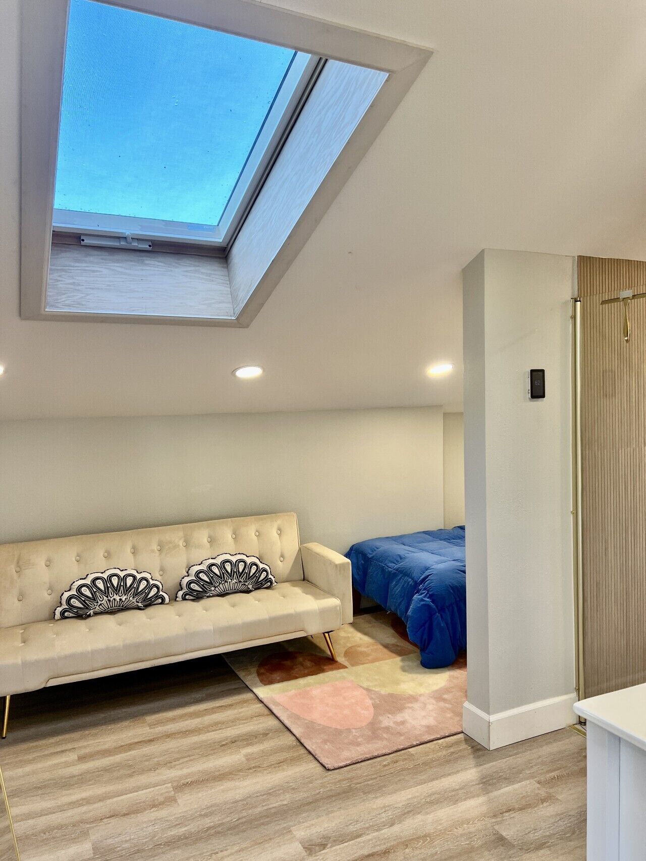 Une pièce dotée d’une lucarne, d’un canapé agrémenté de coussins décoratifs, d’un lit recouvert d’une couverture bleue et d’une armoire en bois.