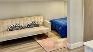 Een kamer met dakraam, een bank met decoratieve kussens, een bed met blauw beddengoed en een houten garderobe.