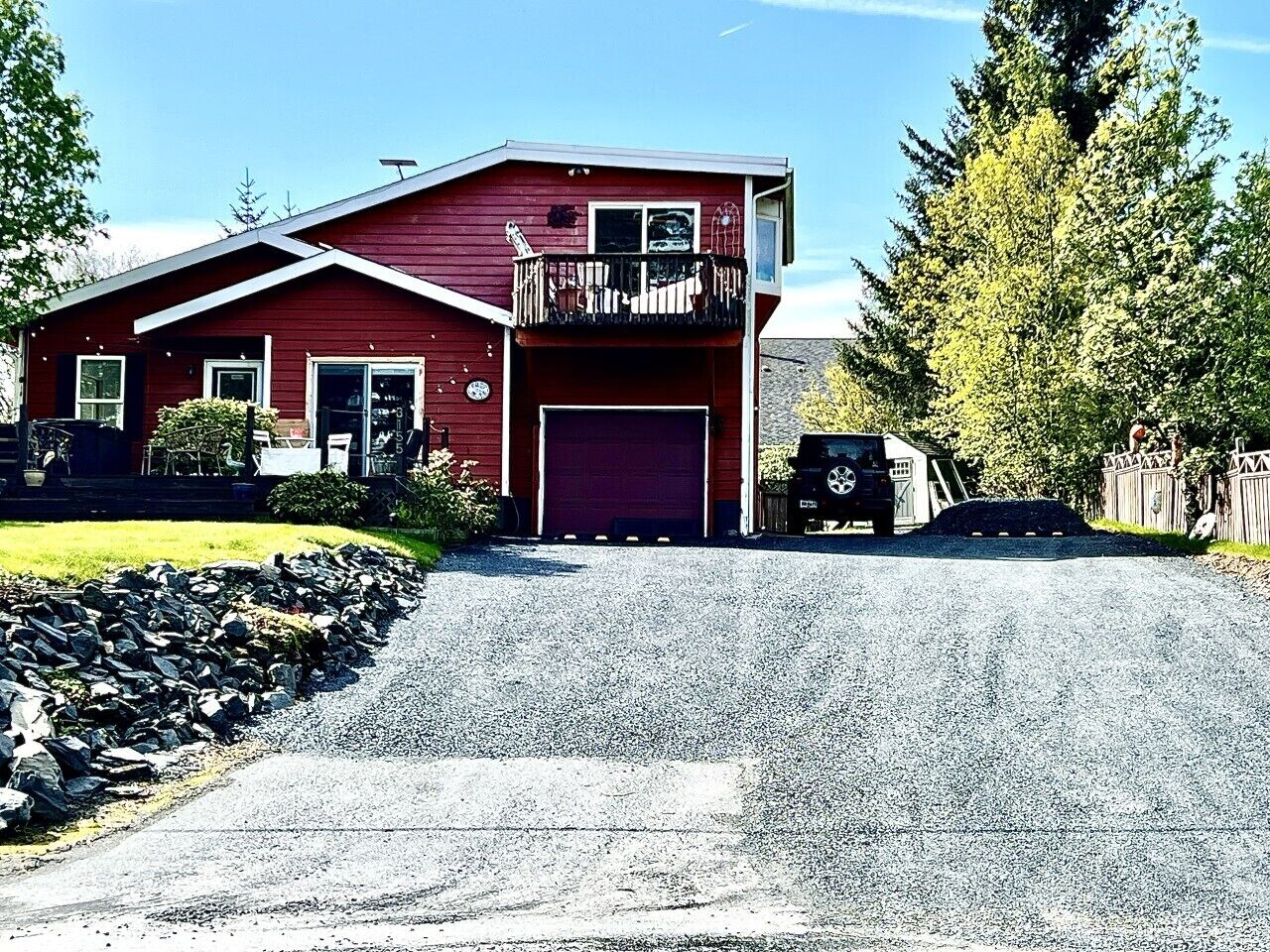 Une maison rouge à deux étages, avec un garage, un balcon et une allée.