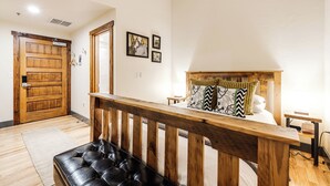 Quarto com cabeceira de madeira, um banquinho de couro preto e porta de madeira.
