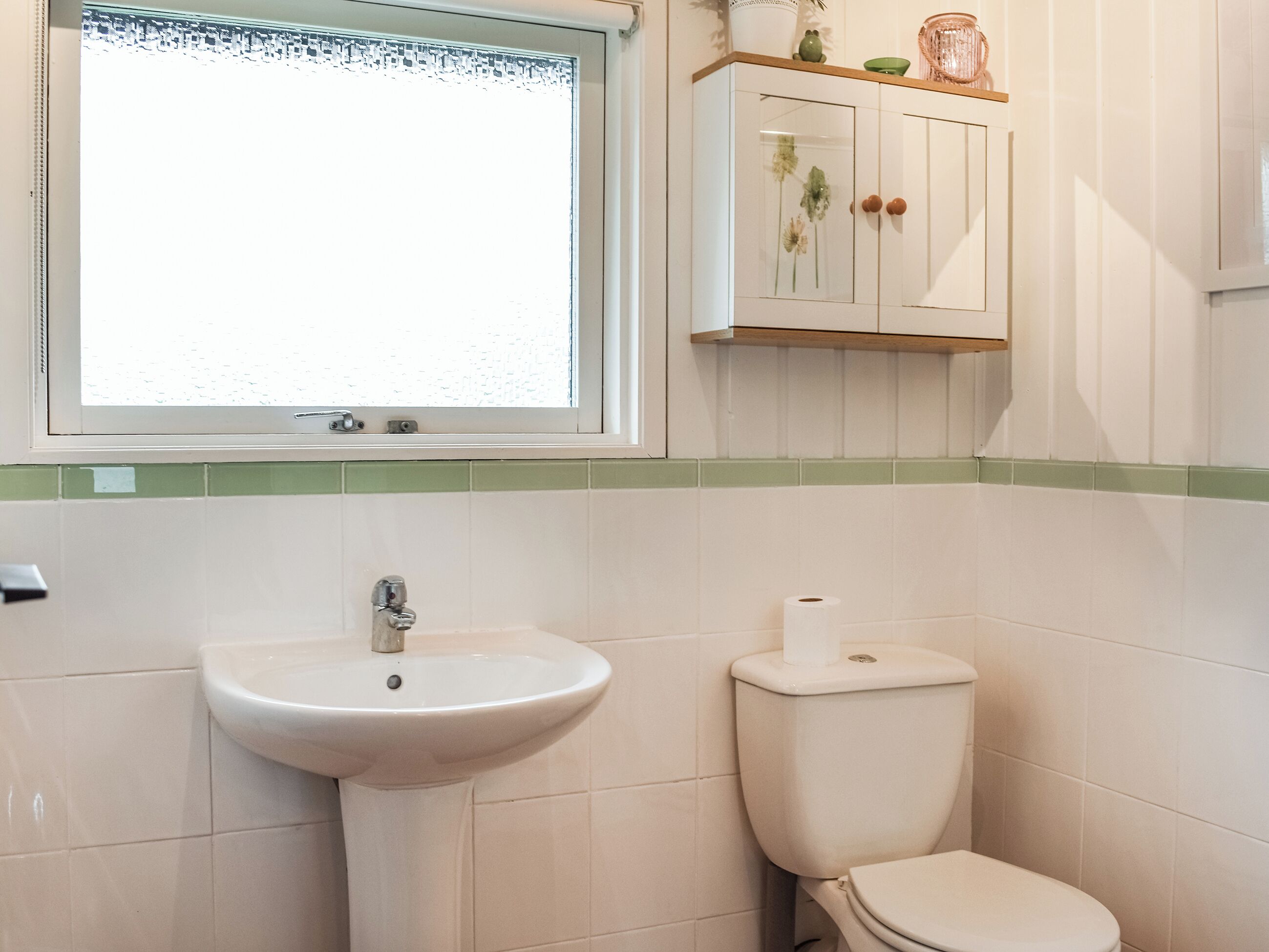 A bathroom with a sink, toilet, and a cabinet above the toilet.