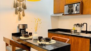 A modern kitchen with wooden cabinets, a black countertop, and a hanging pendant light. - Increible Studio Garden Pool N-B2 (Tulum)