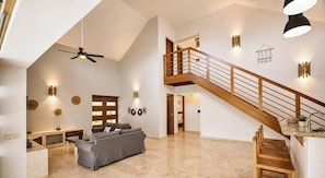 A spacious living area with a high ceiling, a wooden staircase, and a modern kitchen.