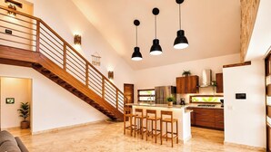 Una cocina amplia con una isla central, una escalera de madera e iluminación colgante.