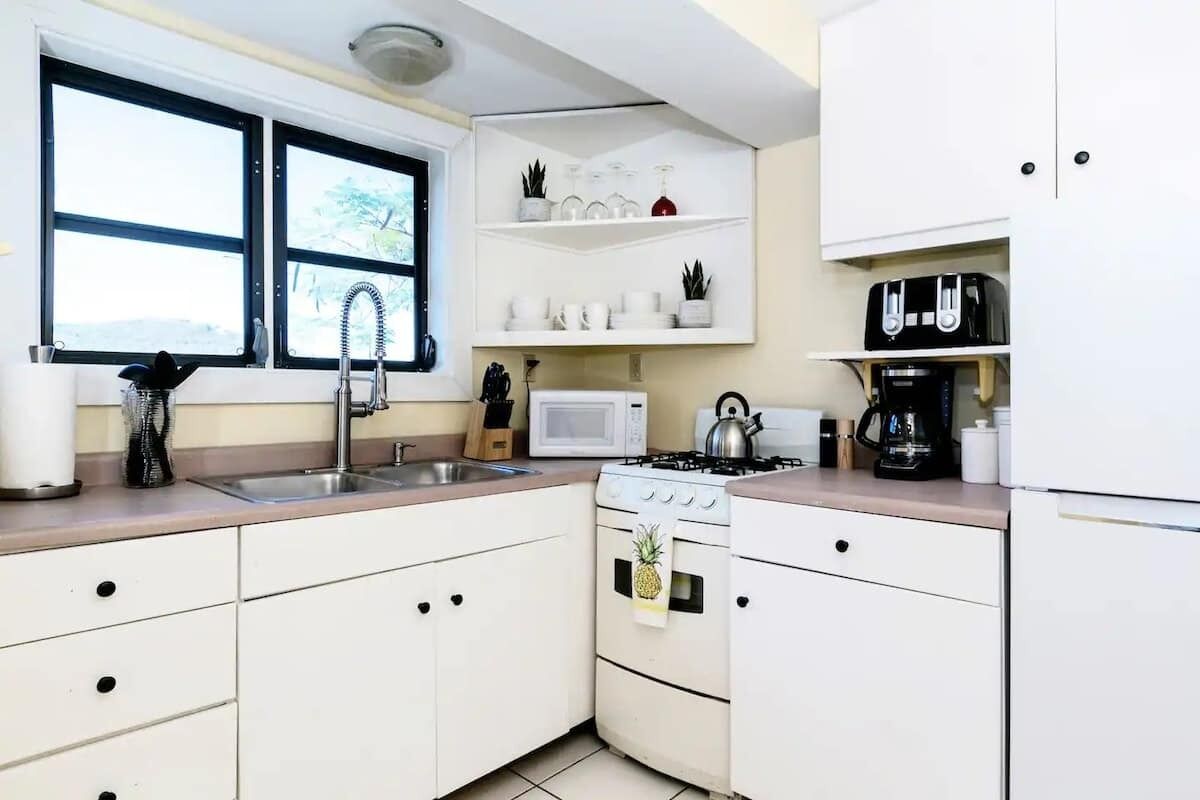 Une cuisine de taille réduite, avec des meubles blancs, une cuisinière, un four à micro-ondes et un évier.