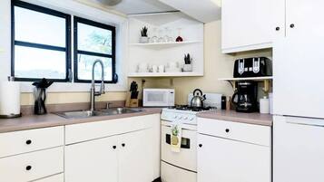 Une cuisine de taille réduite, avec des meubles blancs, une cuisinière, un four à micro-ondes et un évier.