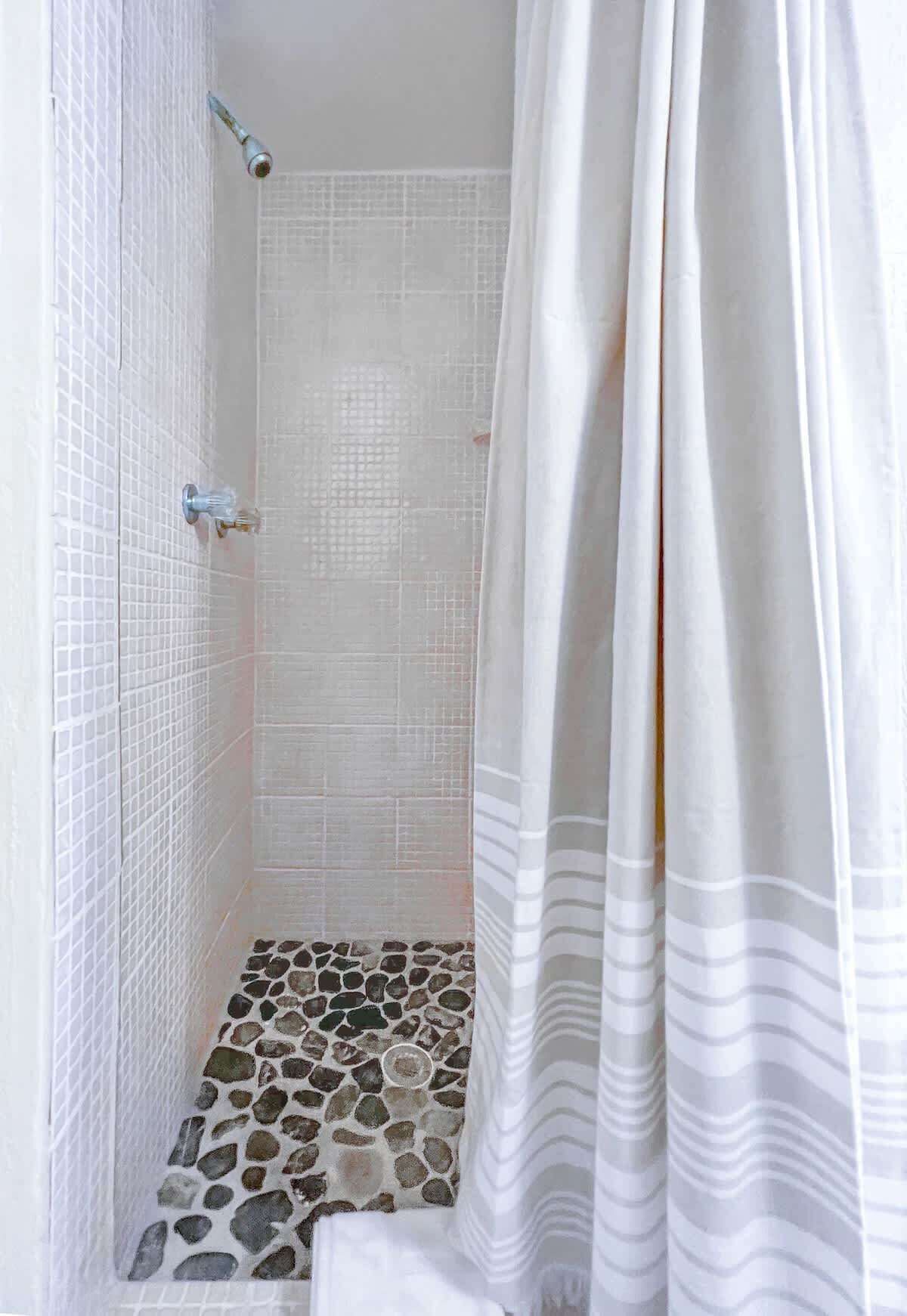 A shower area with white tiled walls, a showerhead, and a stone-patterned floor.