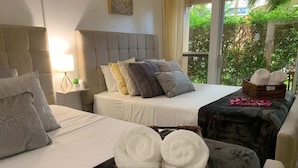 A hotel room with two beds, a sitting area, and a view of greenery outside.