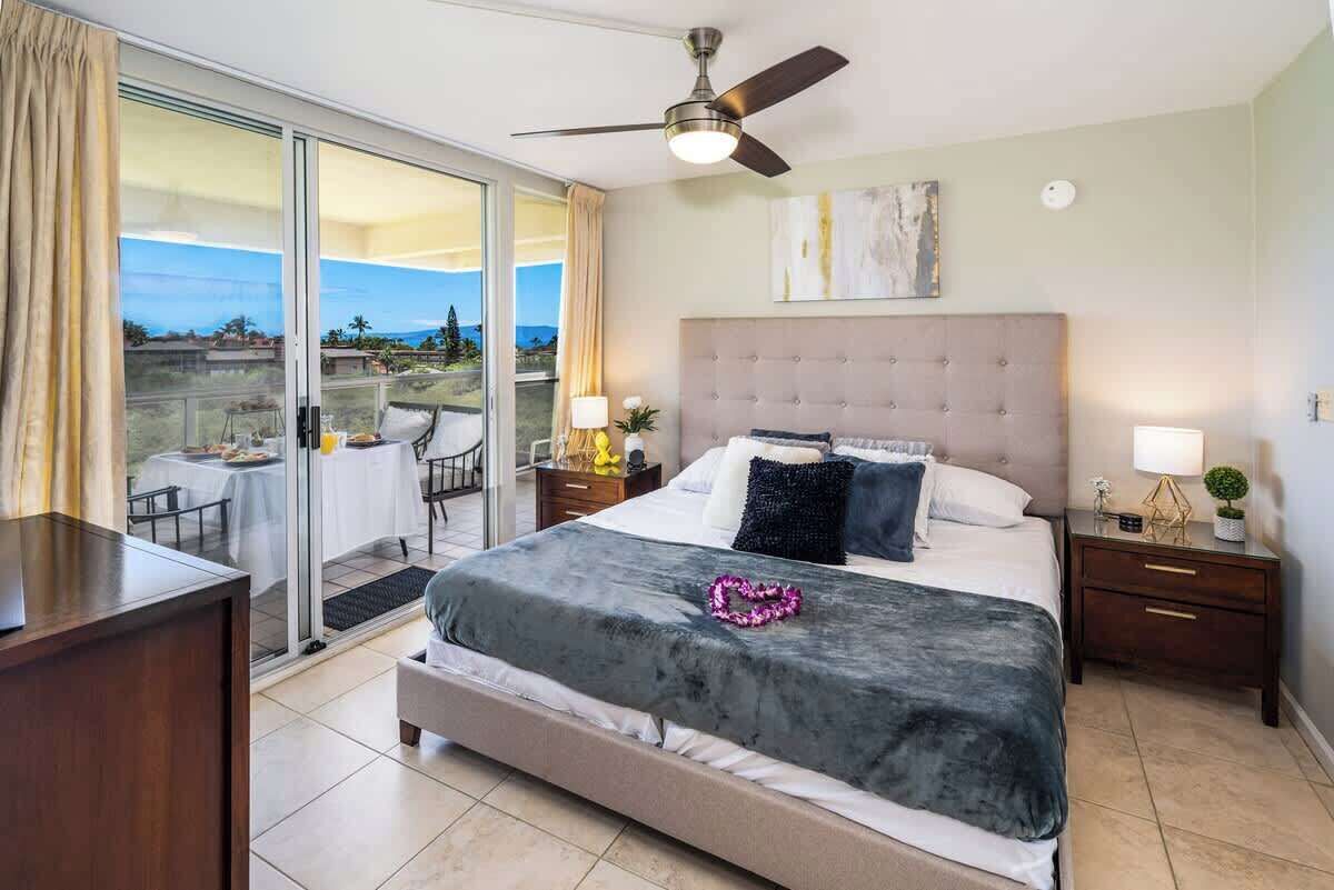 Un dormitorio con una cama grande, un ventilador de techo, vistas a un espacio exterior a través de una puerta corrediza de vidrio y una mesita de noche con lámpara.