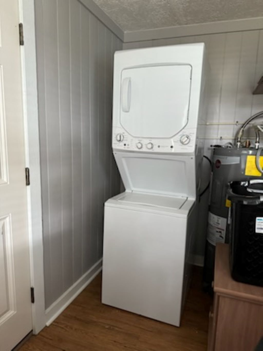 A compact laundry room with a front-loading washer and dryer, a water heater, and a wooden cabinet.