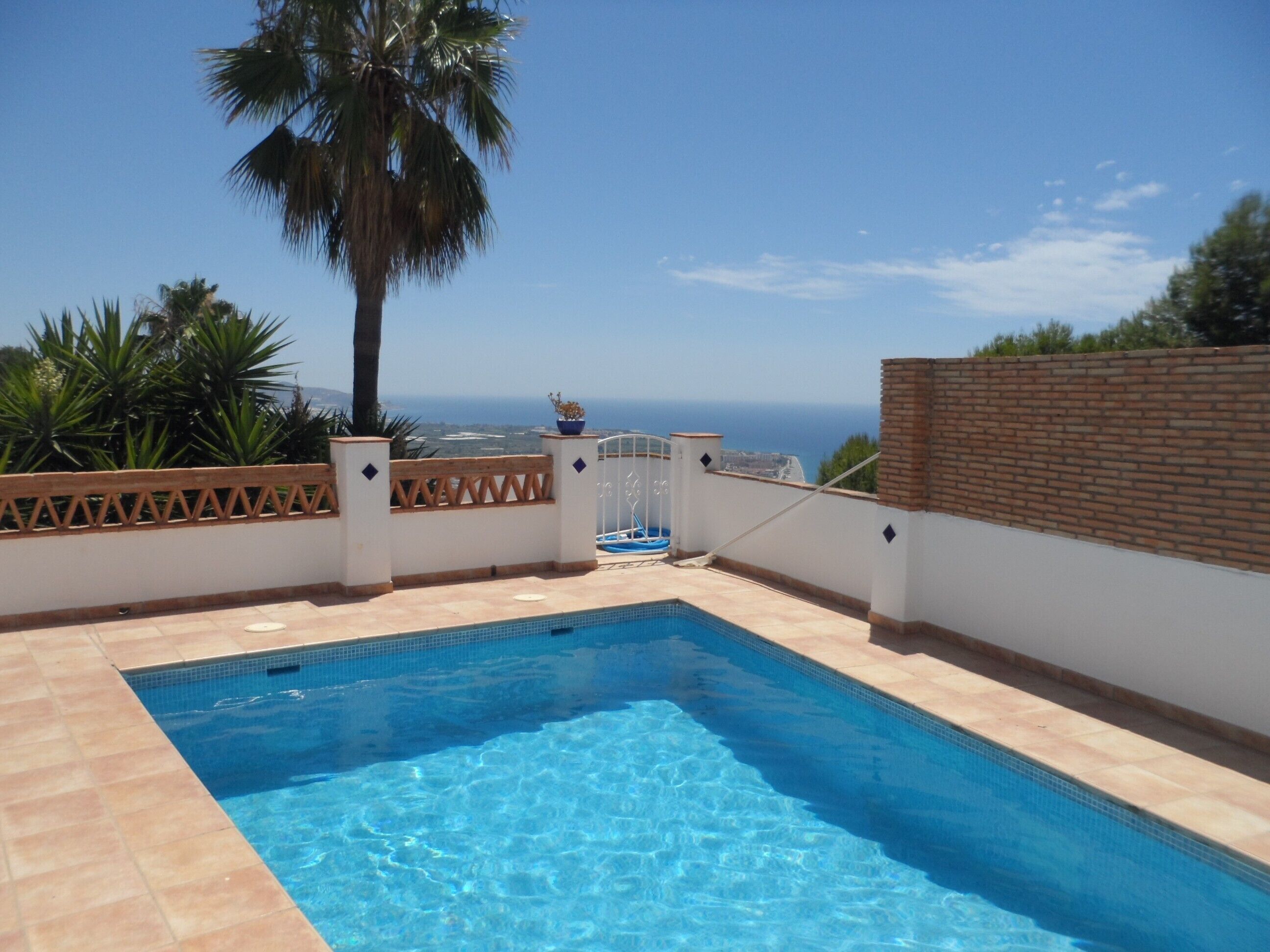 Una piscina con vista sul mare, circondata da un muro bianco e un recinto in legno.